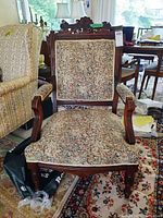 Front view of wood framed arm chair with floral upholstered seat and back, showing carved wood details on the backrest.