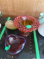 Three art glass dishes displayed: red pedestal lace bowl, purple heart-shaped candy dish, beige shell-shaped dish.