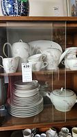 Full cabinet view showing plates, cups, teapot, creamer, sugar bowl, and platter with pink sheaf floral design