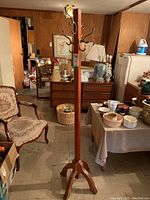 Full view of the wood pedestal coat tree standing upright, showing overall height, hooks at the top, and the surrounding basement environment.