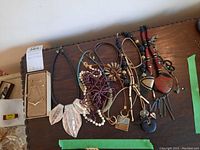Lot of costume jewelry necklaces shown on a dark wooden surface, including a large statement necklace with three pink leaf-shaped pendants, fake pearl necklace, and other beaded and cord necklaces with metal pendants.