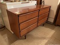 Three-quarter front view of walnut veneer dresser on tile floor beneath appliances