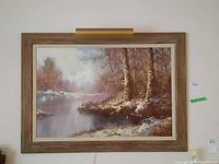 Frontal view of the framed painting hung on a wall with lighting from above, showing the full artwork and frame.