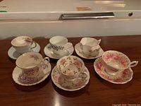 Photo showing set of six porcelain teacups and saucers in various floral patterns on a wooden surface.