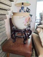 Side view of the hand painted ceramic pot on wooden stand beside stone wall and furniture