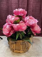 Front angle showing the deep pink faux peonies densely arranged in the woven basket with a handle.