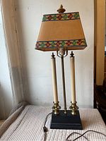 Full view of candlestick lamp with black base, brass candle holders, faux candles and painted shade