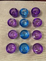 Top down view showing 12 glass candle holders arranged in rows on neutral surface. 4 are blue and 8 are purple.
