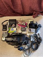 Overall view of three digital cameras, Sony Handycam camcorder, accessories including cases, memory cards, cables, remote, charger, and original box for Handycam