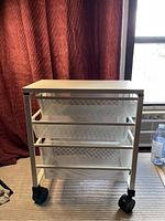 View of white Elfa drawer unit from the side, showing three mesh drawers and black caster wheels.
