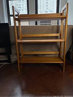 Front view of folding bookcase showing all three shelves and light oak wood frame against a window background.