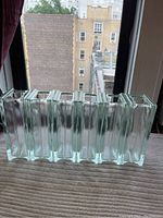 Six glass bricks or rectangular vases placed side-by-side, showing their tall rectangular form and transparent nature with light green tint.