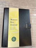 Front view of black leather-like cover with yellow paper label 'Memory Box Journal' and brand mark 'Kates Paperie'
