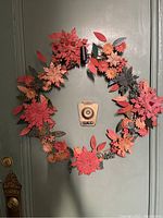 Front view of metal floral wreath hanging on a door showing detailed layered petals in orange, yellow, and green with an aged look and slight rust.