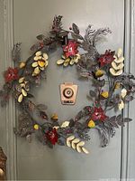 Full view of the metal wreath hanging on a door showing the arrangement of leaves, flowers, and acorns.