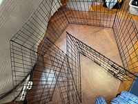 Black metal wire pet enclosure panels arranged on wooden floor showing multiple panels and the door with latches