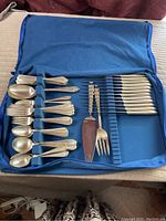 Full flatware set arranged in blue silversmith cloth cover showing knives, spoons, forks, and serving pieces.