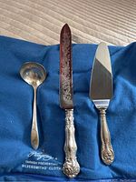 All three pieces of vintage silver plated cutlery displayed on a blue silversmith tarnish-preventing cloth showing detailed design of handles and blade.