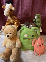 Photo showing all seven plush toys including giraffe, owl and hedgehog finger puppets, T. rex, small pink and medium green ugly dolls, and a teddy bear.