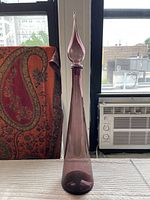 Front view of tall purple genie bottle with stopper, showing tapered shape and pointed stopper.