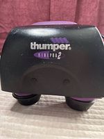 Front view showing brand and model 'Thumper Mini Pro 2' on black plastic body with purple details.