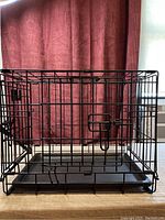 Front view of black metal dog training crate closed, showing front door and plastic slide-out tray.