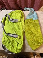 Photo of two light green nylon bags: a duffel bag with adjustable grey straps and smaller shopping bag with blue shoulder strap and felt patch.