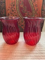 Two red glass vases side by side showing the front and the swirl design with flared rim.