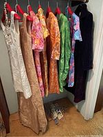 Seven retro dresses including cream textured, peach, orange floral, green, pink tie-dye, and a dark purple coat, hanging on multi-colored plastic hangers.