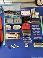 Full lot overview showing eyeglasses, watches, cufflinks, and pocket cutting tools, displayed on a blue tabletop.