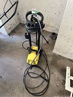 Full view of Karcher 390 pressure washer showing yellow and black body, hose coiled on top and spray gun resting on unit on concrete floor.