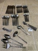 Full layout of all cutlery pieces included in set on tile floor, showing knives, forks, spoons, and serving utensils