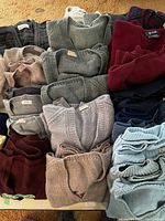 Multiple folded sweaters laid out showing range of colors from gray, beige, burgundy, navy, and light blue, some featuring detailed knit patterns.