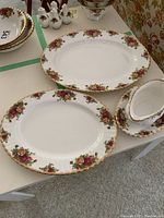 Top down view of two oval platters and one gravy boat with tray, all featuring floral rose pattern with gold trim.