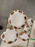 Top-down view of two large round floral serving dishes with scalloped gold trim and several smaller dishes with similar floral and gold trim design on a white table.