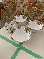 Three Royal Albert Old Country Roses footed bowls arranged on a table with two sets of matching salt and pepper shakers nearby, showing the floral pattern and gold trim.
