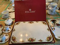 View of red Royal Albert box, medium and large floral trays, candlestick holders and butter dish, teacups in background
