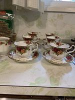Front view showing six teacups on saucers with the floral rose pattern and gold trim in a kitchen setting.