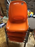 Stacked view of four dark orange fibreglass chairs with chrome metal legs displaying overall condition and stackability.