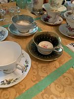 Photo showing multiple fine china teacups and saucers with floral designs and gold detailing