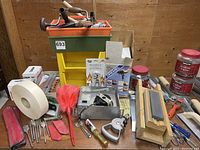 Overall view of assorted hand tools, Dremel shaper rotor table packaging, sharpening stones, and various small tools and accessories on a wooden table.