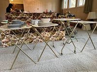 Four portable tables with folding metal legs and trays on top, situated in living space with floral furniture.