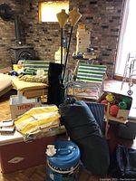 Wide shot showing multiple vintage camping and patio items including coolers, chairs, tiki torches, lanterns, and water dispenser.