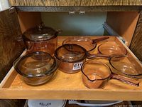 Full set of Visions glass cookware including pots, pans, and baking dish arranged in drawer showing amber translucent glass with lids and handles.