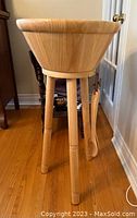 Side view of the wooden salad bowl on four-legged stand with serving utensils hanging on the side.