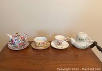 Side view of all four tea sets showing teapots and cups on a wooden surface