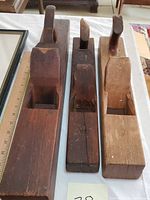 Three antique wooden woodworking planes arranged side by side on a table, showing the top and side views, highlighting their wooden bodies and handles.