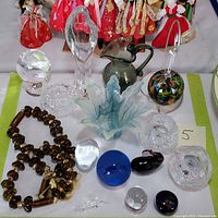 Top-down view showing the collection of glass figures, paperweights, necklace and candle holders on a white base with a green border.