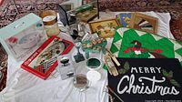 Wide view showing entire lot including breadbox, foot spa, various art pieces, Christmas decorations, and kitchenware arranged on white cloth