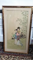 Full frontal photo of the framed Chinese watercolor painting showing two young women in traditional clothing standing on grass with bamboo and rocks in the background.